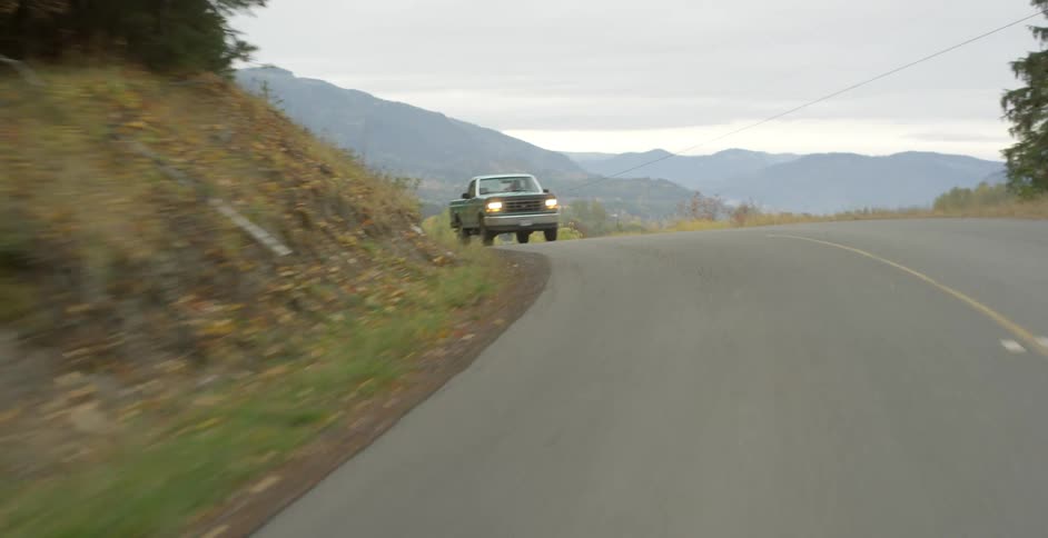A truck drives on a road past a farm in a rural area