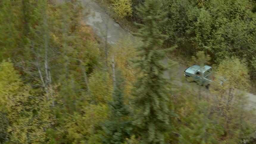 A truck with a bike in the back drives along a dirt road