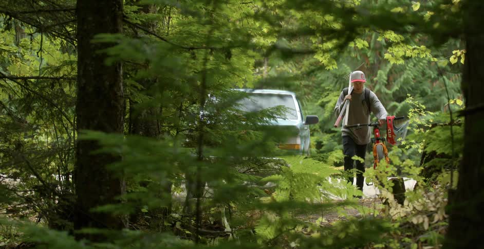 A white male walks into the woods with some tools and a bicycle in tow