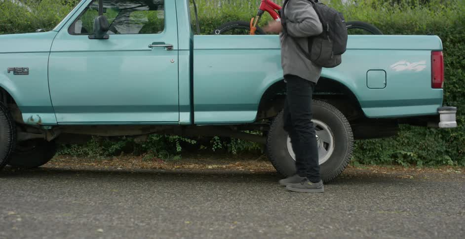 A male pushes a bicycle towards a truck and puts it in the bed