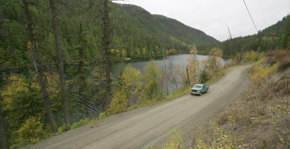 A truck with a bike in the back drives past a lake