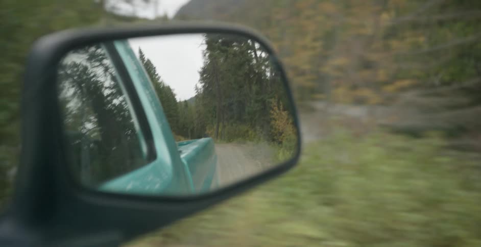 A green pickup truck drives down a dirt road that runs parallel to a river