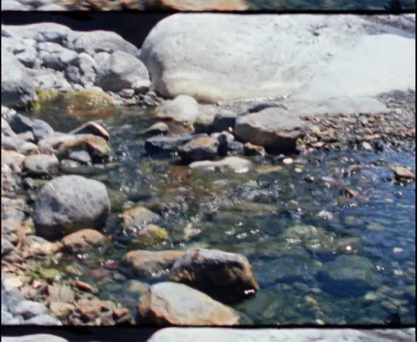 A small stream running between boulders and over small rocks in the wilderness