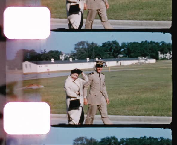 A military officer and an older white woman smile while walking on a military base