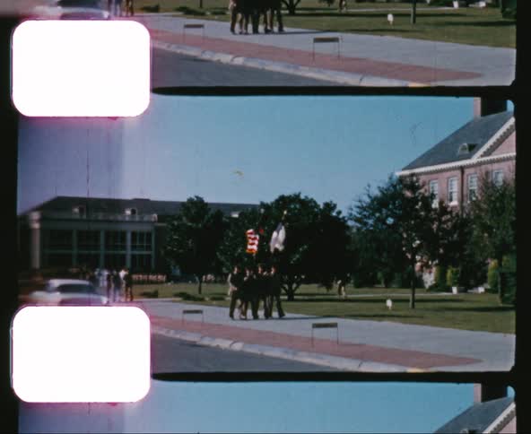 A group of military men bearing flags lead a march on a military base