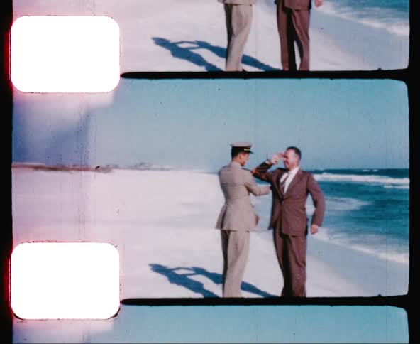 A military officer teaches a civilian how to salute while standing on the beach