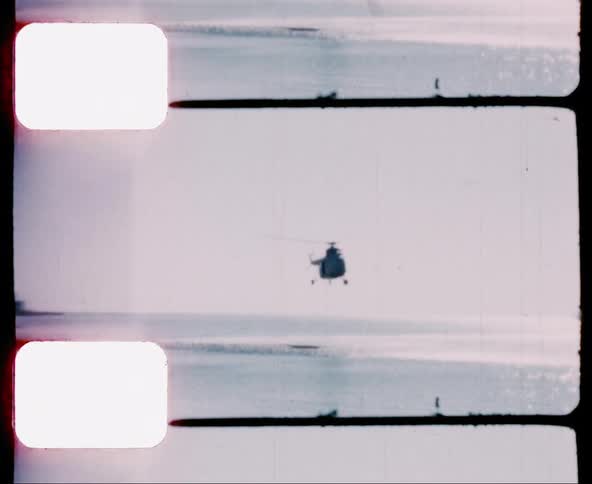 A helicopter spinning while hovering over the ocean just off the coast of a beach