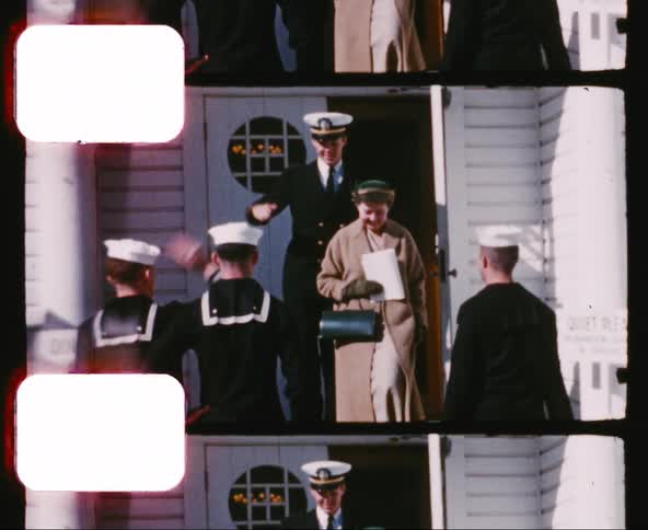 Sailors salute as a man in a military uniform exits a building along with a woman