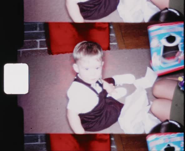 Male baby sits on the floor as his mother takes a toy out of the packaging