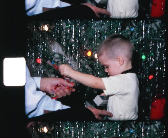 Vintage footage of excited little boy opening present with dad next to christmas tree