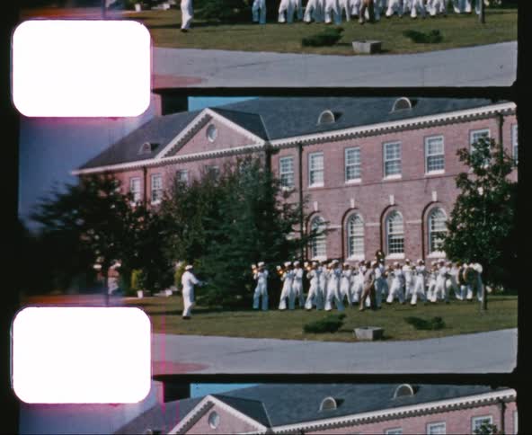 A navy band marches with their instruments on a yard outside a building