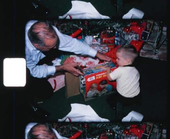 An old man helping a young boy to open the package of a toy truck under a christmas tree