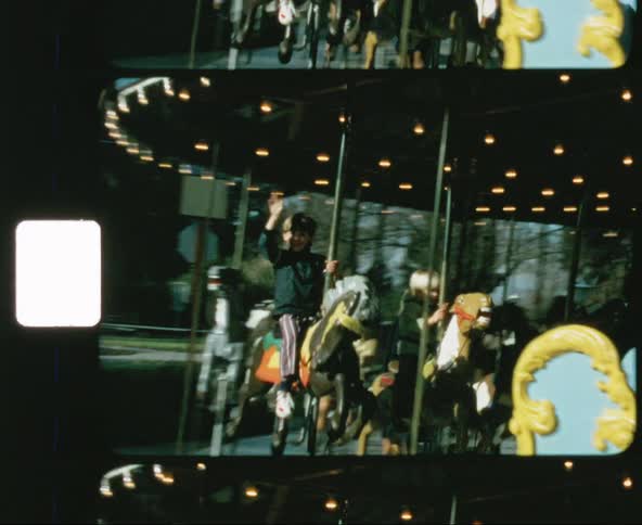 Child in green jacket waves while riding a carousel