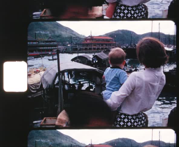 A white woman and her child stand near the shore and look at the boats floating in the marina