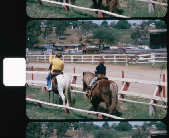 A pair of young boys each slowly riding their own pony together around a horse track