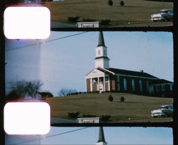 Vintage footage of a car parked next to church with a steeple on a hill