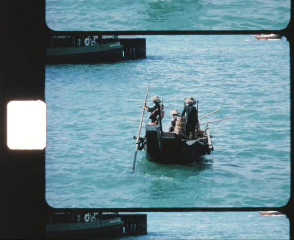 A small boat with four asian sailors floats in a bay