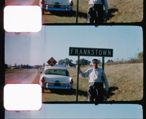 Vintage footage of man standing under a town sign for a photo while traveling