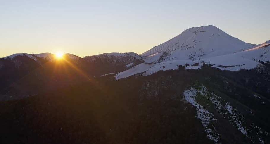 Aerial rising up to the sun setting over a huge volcano