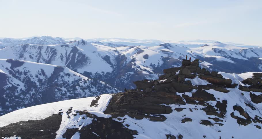 Fast aerial of two people on top of a snowy mountain