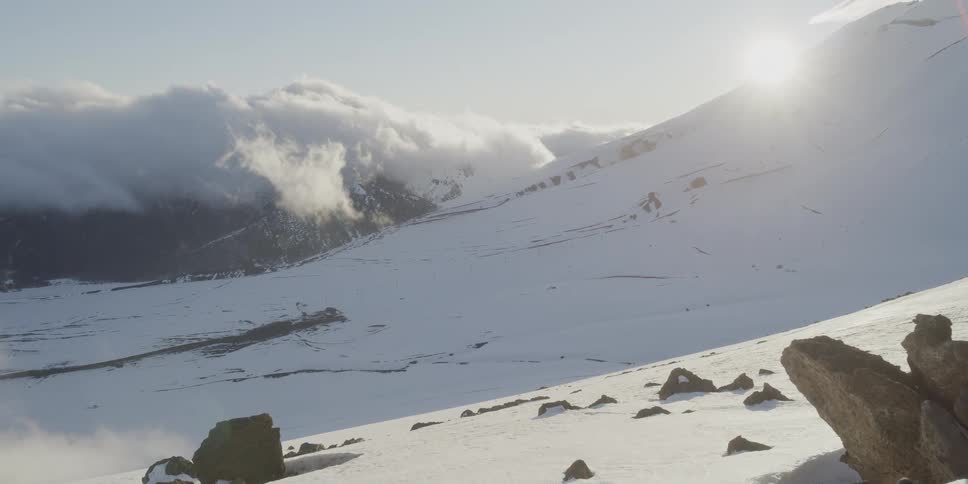 The sun shines and glares on the snow of a mountain slope