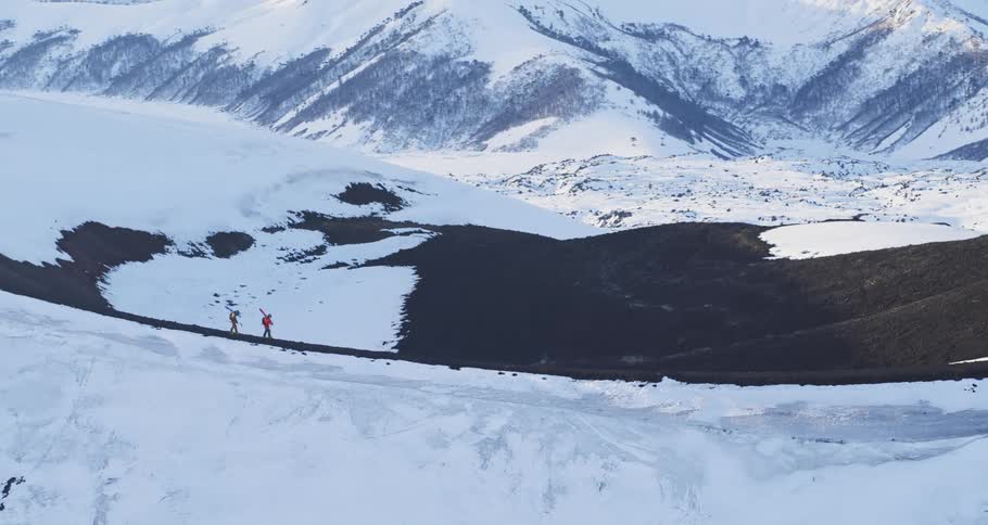 Aerial view of two mountaineers trekking across a snowy ridge