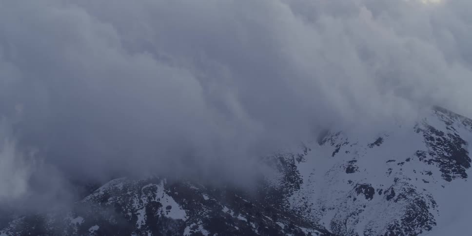 A dense cloud bank moves over snowy mountains