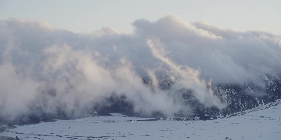 Clouds swirl over a a snow covered mountain at sunset