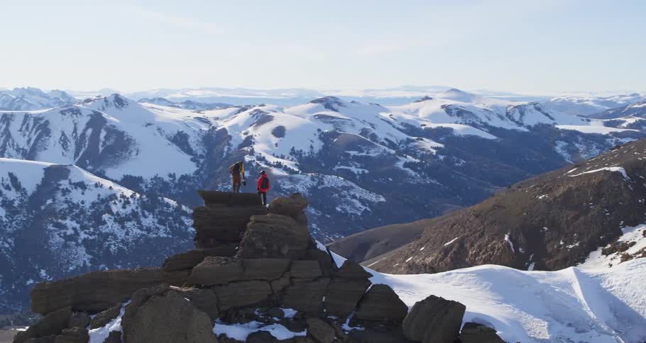 Aerial of two climbers on a ridge in front of a huge mountain range