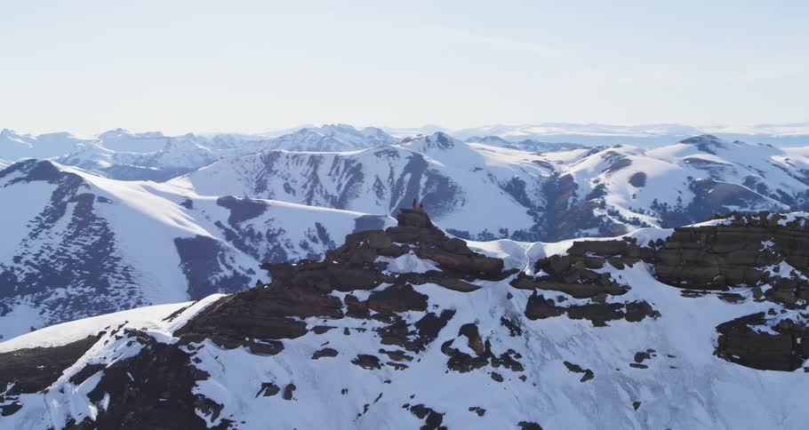 Wide aerial of two people on top of a snowy mountain