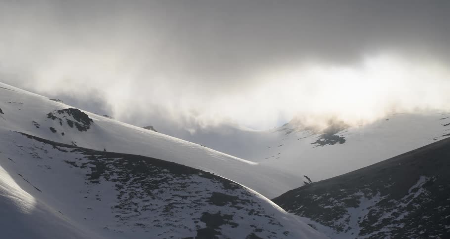 Aerial as dark clouds hang over snow covered sloping hills