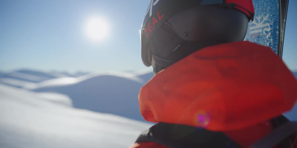 A man holds his skis and looks across the snowy hills