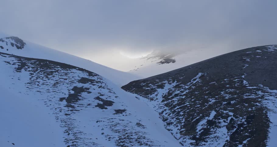 Aerial push on a snow covered mountain slope under a cloudy sky