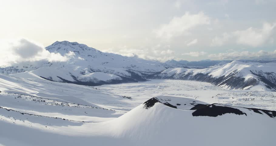 Aerial of volcano cone covered in snow near mountain range