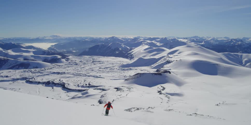 A man skis by the camera into a beautiful valley