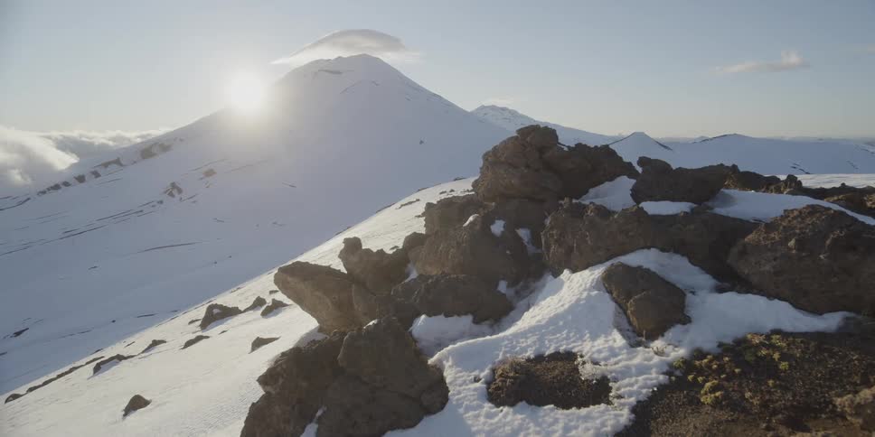 The sun sits on the top of a mountain ridge in winter