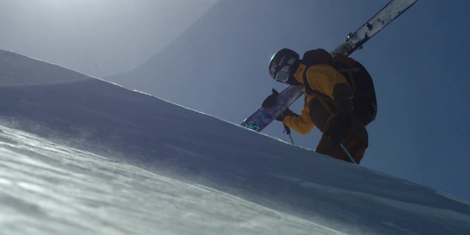Skier carrying skis hiking uphill on a windblown slope