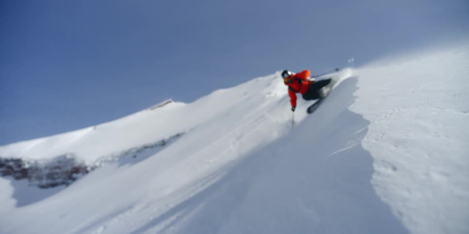 A skier slashes a snowy wind feature
