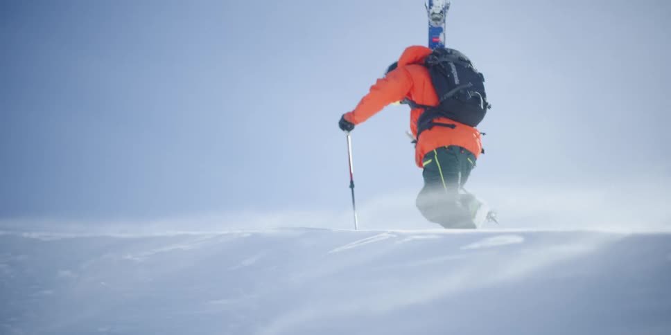 A skier walks up a hill in the blowing snow