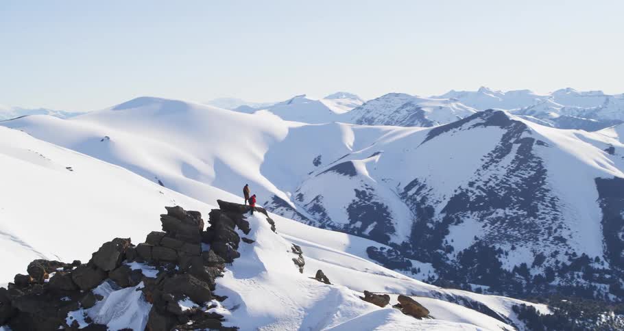 Aerial of two  mountaineers standing atop mountain ridge covered in snow