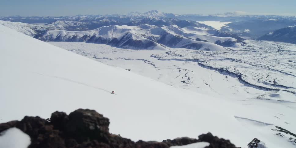 A person is skiing down a huge slope in front of a beautiful valley