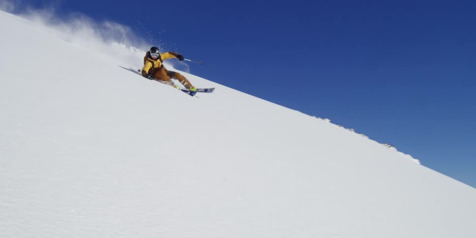 A man skis down a hill on a sunny day past a beautiful landscape