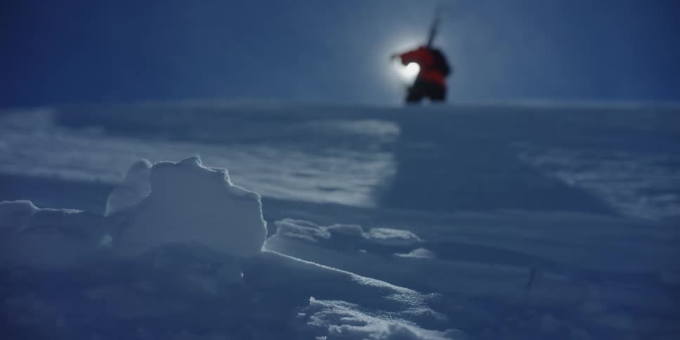 A skier walks across the top of a mountain as snow blows