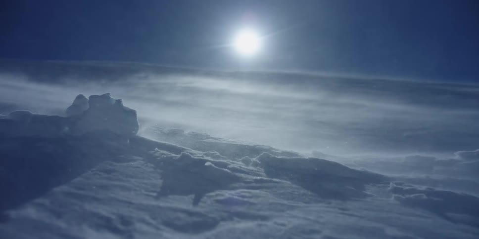 Snow blows heavily across the land as the sun sets