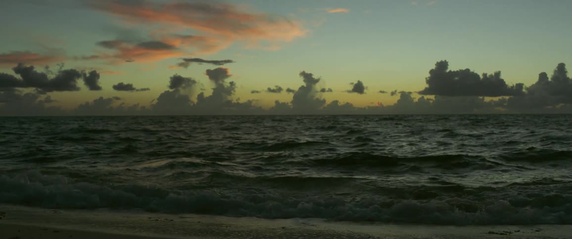 Strong waves crash onto the shore as the sun rises