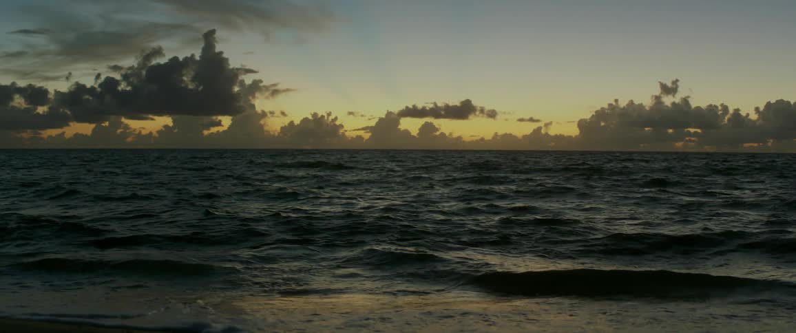 Waves crash on beach with tint of orange on sky near horizon