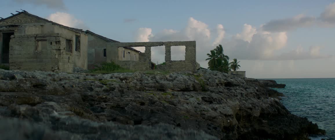 An abandoned dilapidated house sits on a cliff overlooking the water