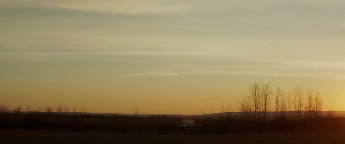 A pickup truck drives through a rural area at sunrise