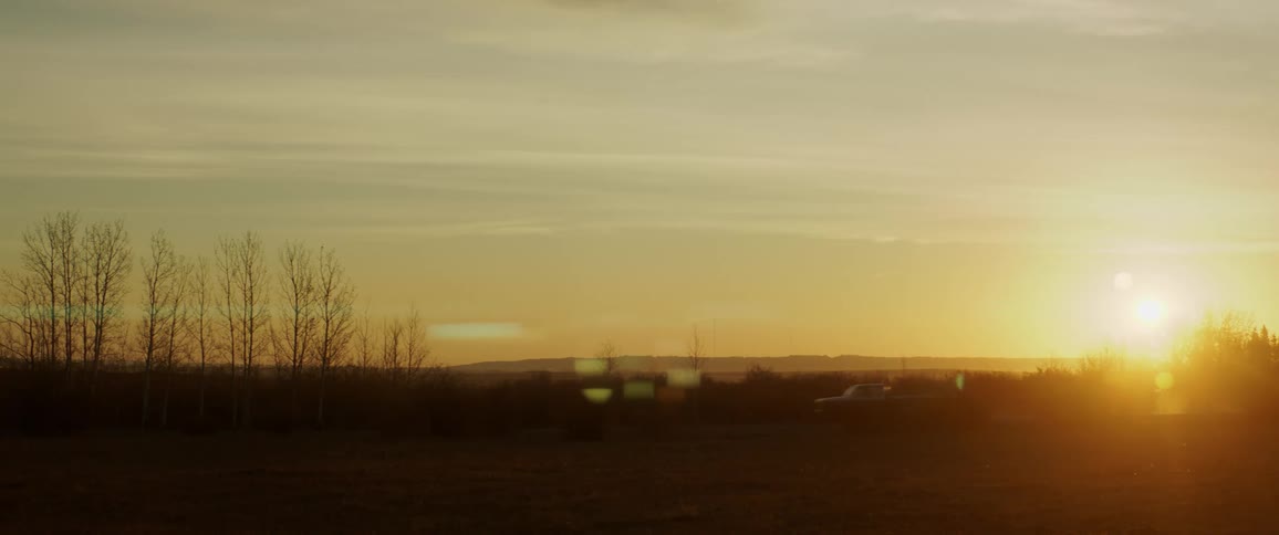 A truck kicks up dust as it drives down a dirt road at sunset