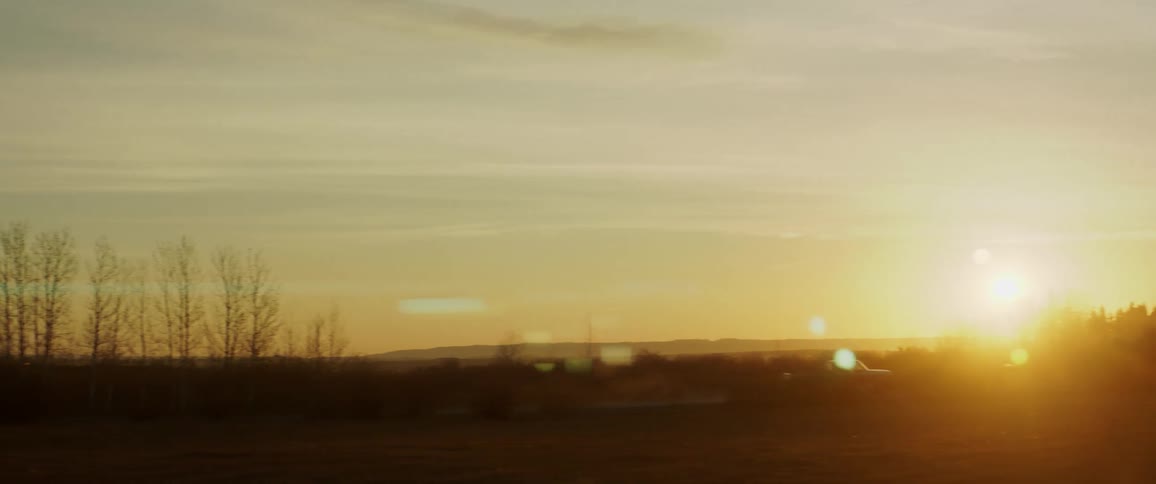 A pickup truck drives through a rural area at sunrise